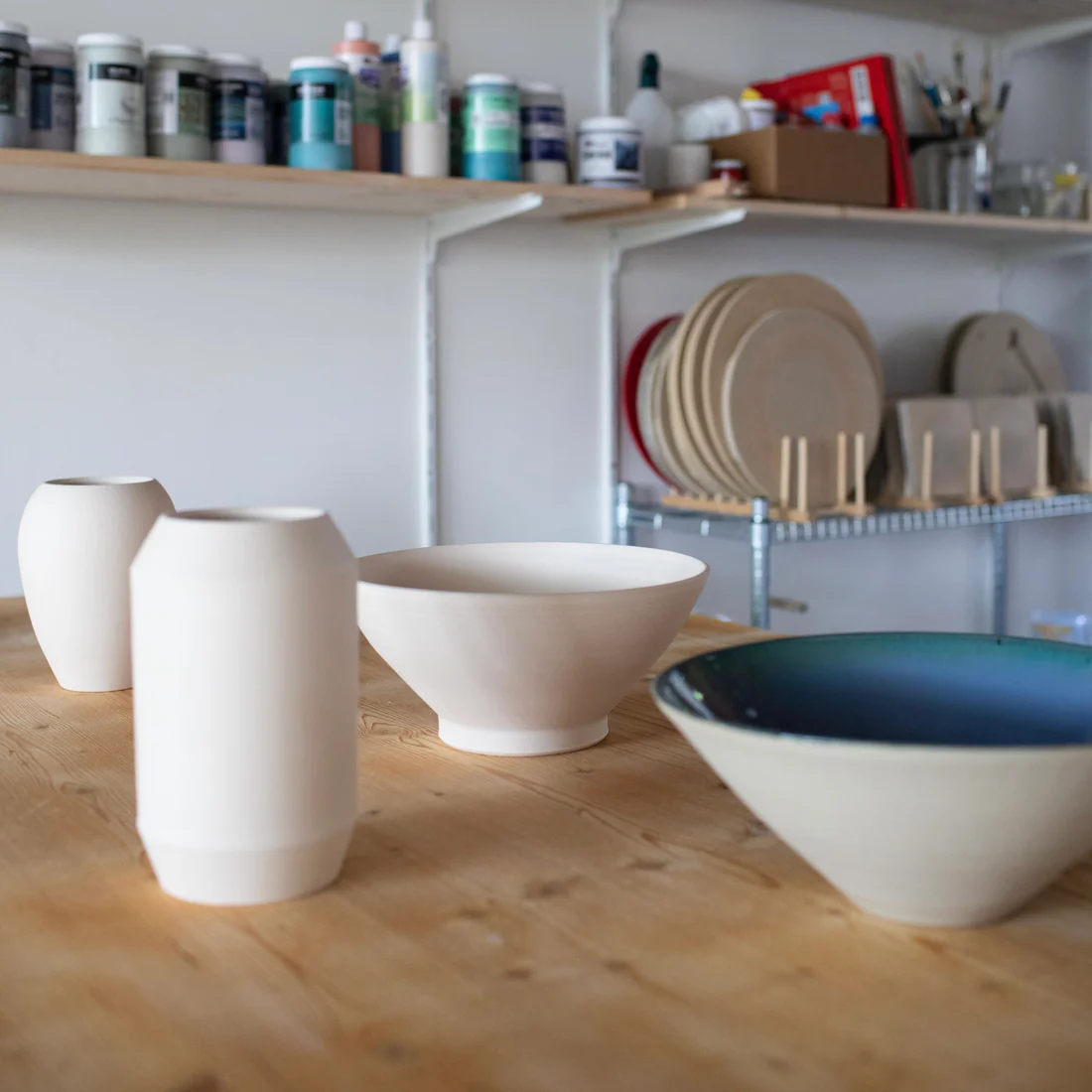 Vasen und Schalen auf der Werkbank im Atelier, im Hintergrund Glasuren und Werkstücke — handgemachte Keramik aus Baden