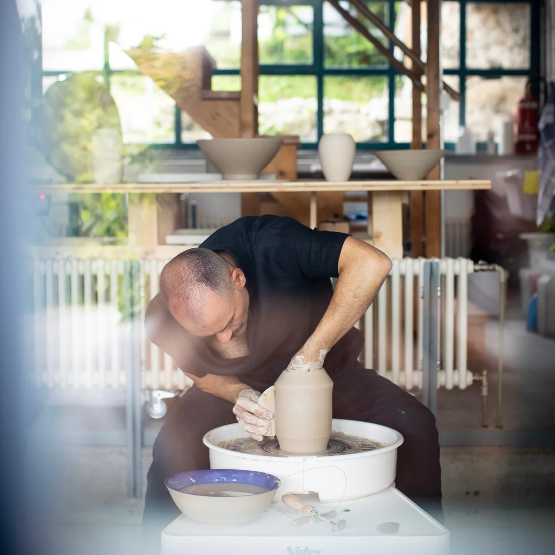 Blick durchs Fenster ins Atelier: Fabiano dreht ein Gefäss an der Töpferscheibe — Inochiceramic in Kirchdorf bei Baden